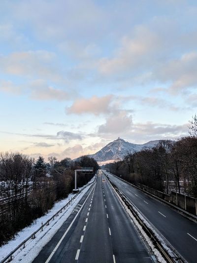 Road leading towards mountain against sky during winter