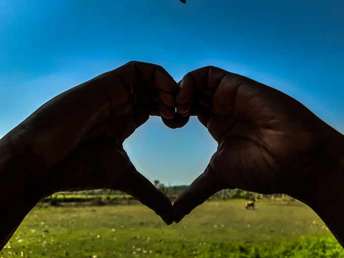 Cropped image of hand holding heart shape against blue sky