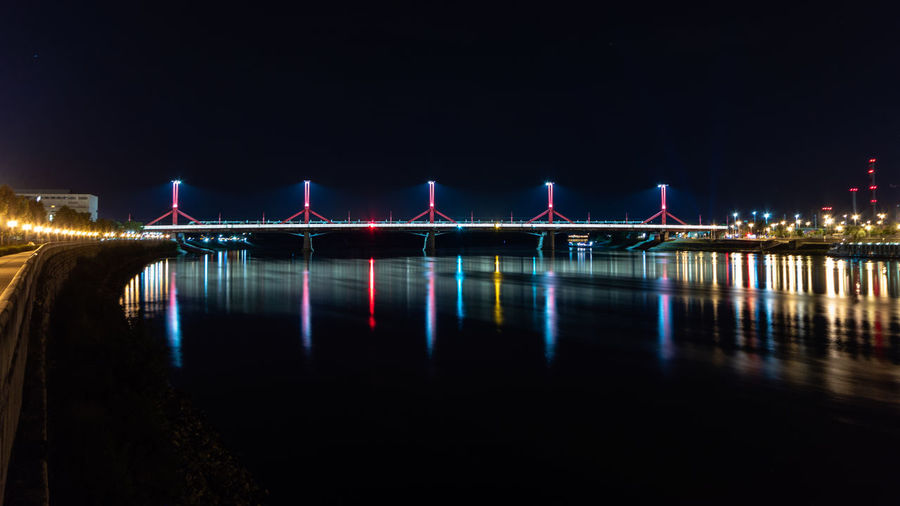Illuminated bridge over river against sky at night