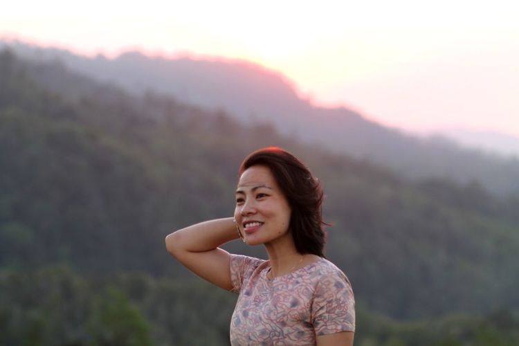 Smiling woman looking away against mountains during sunset