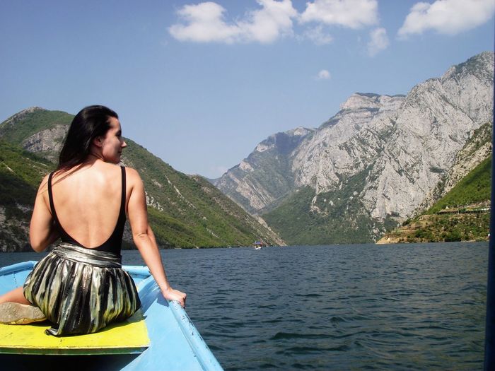 Rear view of woman sitting in boat at sea against mountains