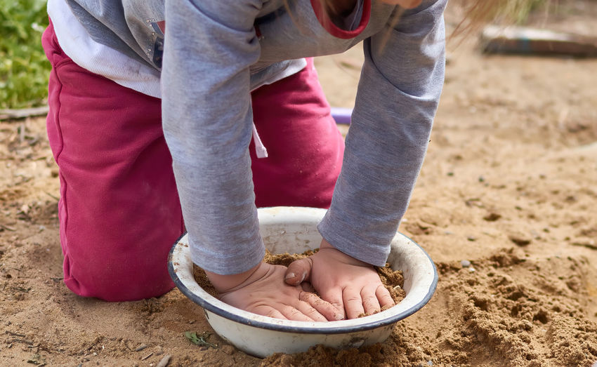Closeup of a child hands, playing in the sand with metal dish in village area