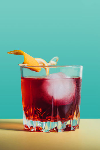 Glass of bitter alcoholic negroni cocktail served with ice and orange peel on light surface