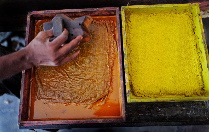 High angle view of worker holding printing block next to color container