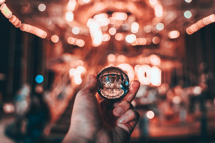 Close-up of hand holding crystal ball against illuminated amusement park ride
