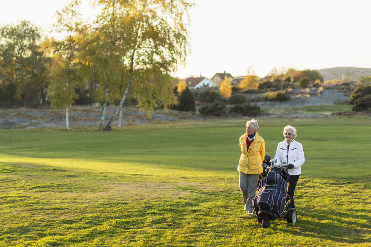 Senior female friends walking with golf bags on course