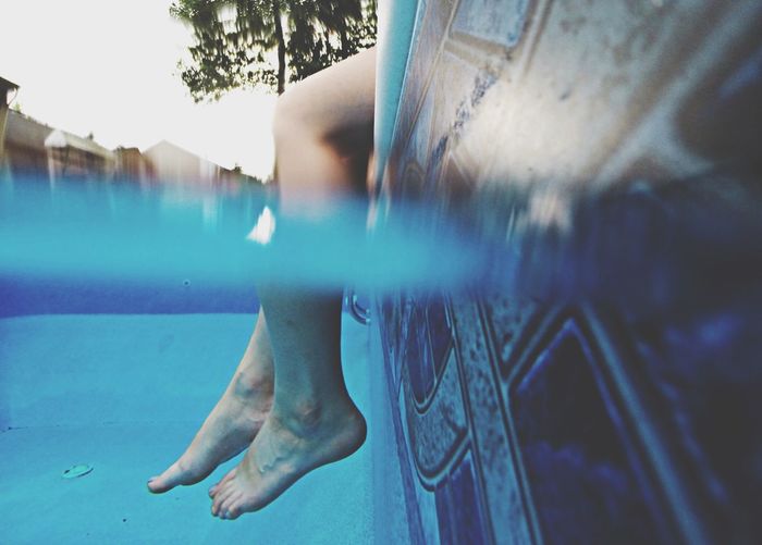Cropped image of legs dipped in swimming pool
