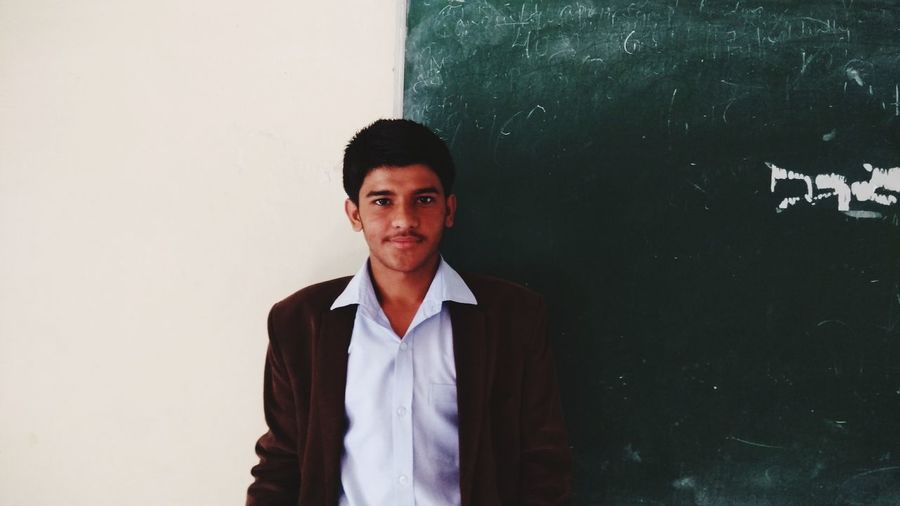 Portrait of male student standing by blackboard in classroom