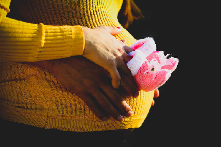 Midsection of man and woman holding baby booties over abdomen