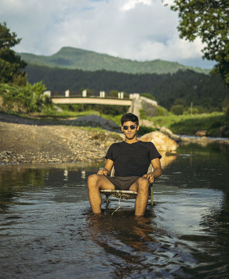 A young handsome asian boy sitting in a chair in the middle of a river with black sunglasses