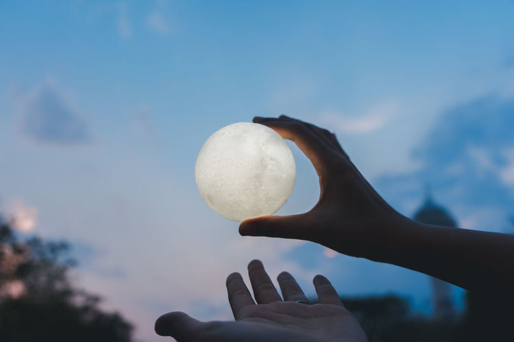 Cropped hand of person holding illuminated ball against sky