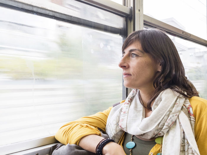 Woman looking through window while sitting at train