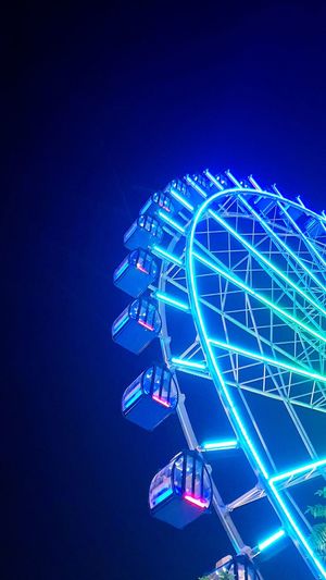 Low angle view of illuminated ferris wheel against clear blue sky