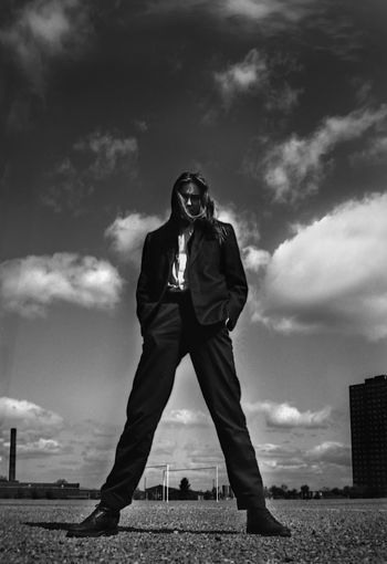 Low angle view of man in suit standing on road against cloudy sky