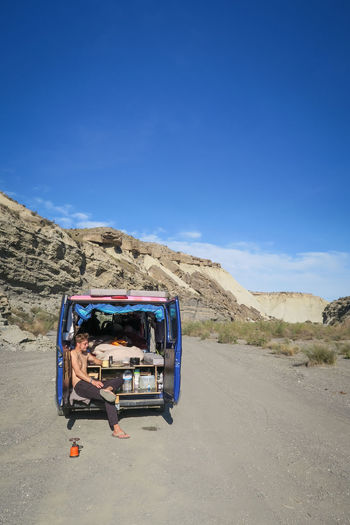 Shirtless man sitting in land vehicle on road against mountains