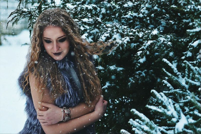 Woman wearing fake fur standing by tree during snowfall