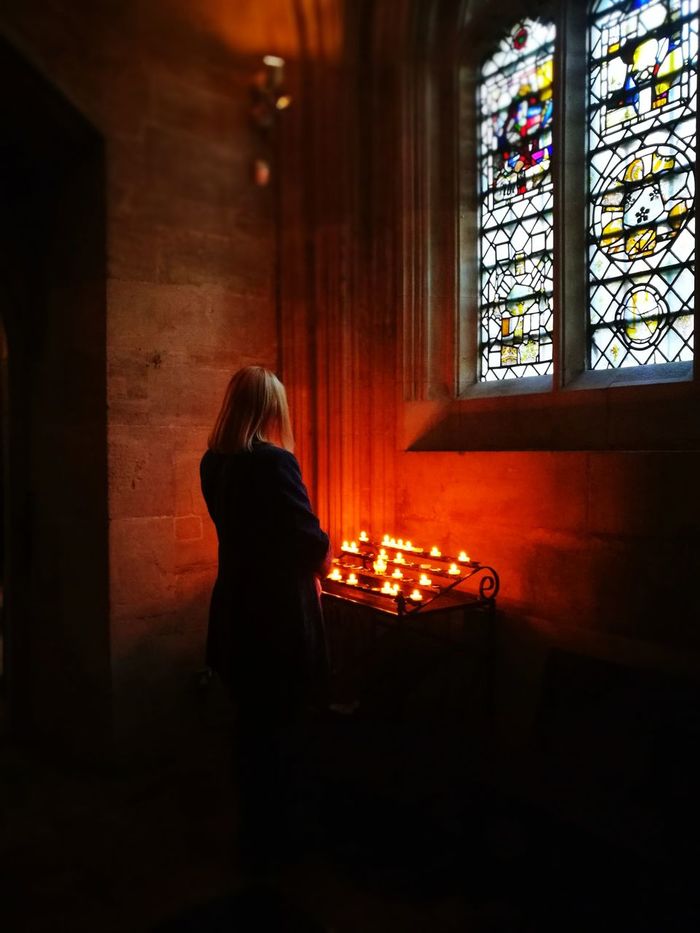 Woman sitting by illuminated candles and window in church