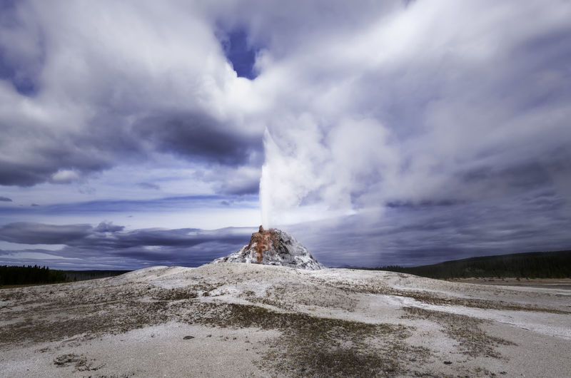 Steam emitting from geyser against cloudy sky
