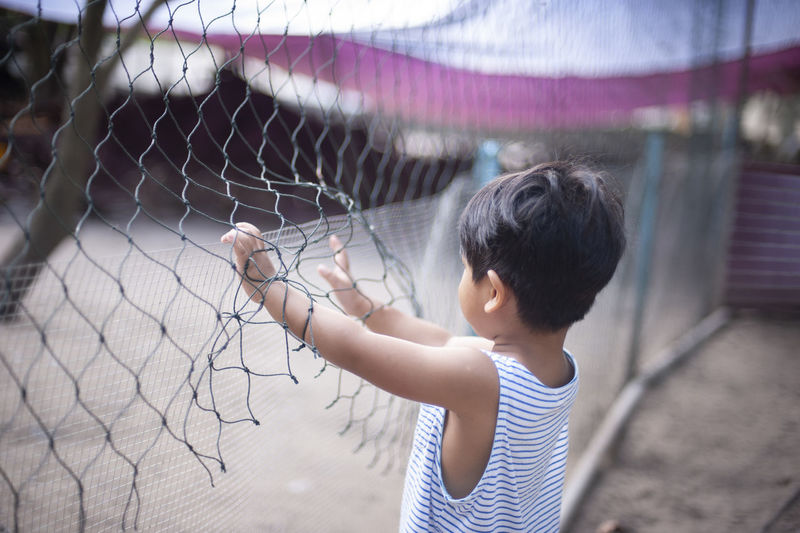 Boy standing by chainlink fence