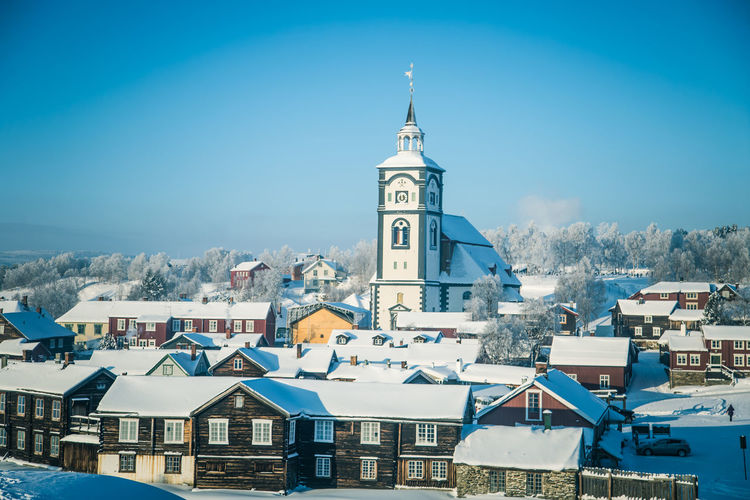 High angle view of church amidst houses against clear blue sky during winter