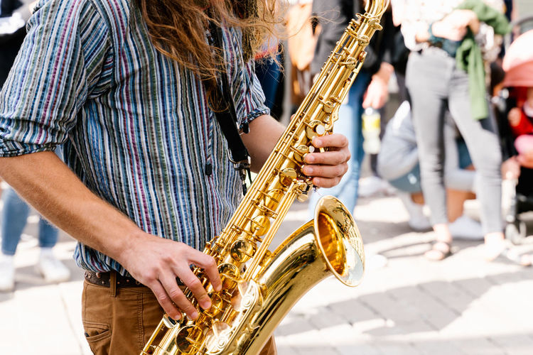Hands of a young man with long hair playing saxophone in a crowded the street