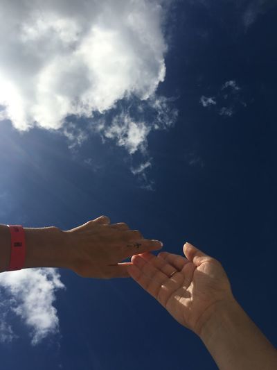 Low angle view of hand holding umbrella against blue sky