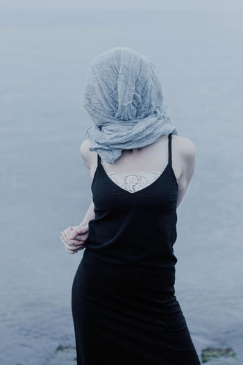 Woman covering face with scarf while standing by sea