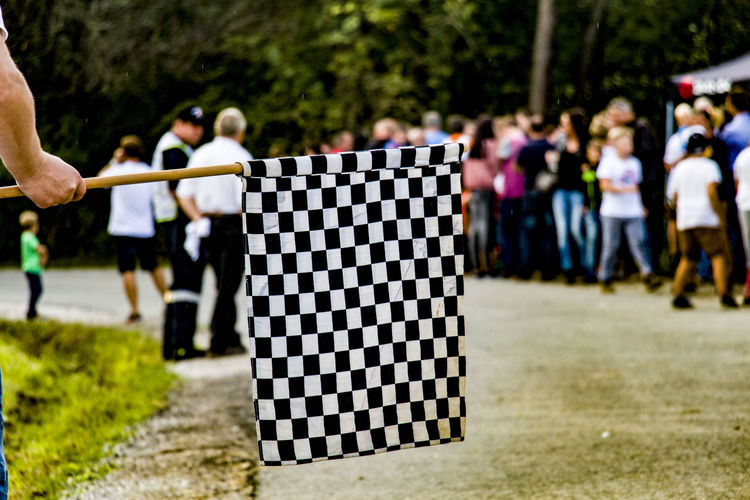 Cropped hand of man holding checkered flag against people