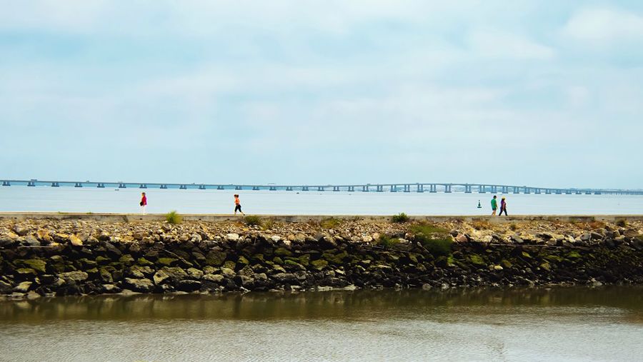 Tilt-shift image of people on pier at tagus river against sky