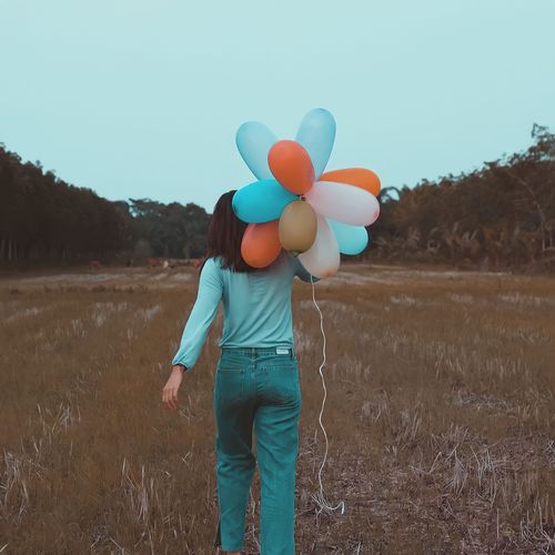 Rear view of woman holding balloons against sky