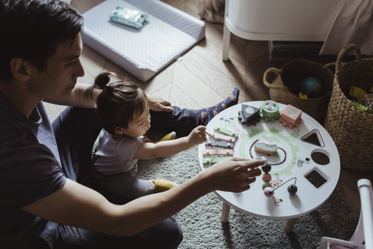 Male toddler and father playing with geometric toy at home