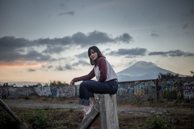 Portrait of young woman sitting on mountain against sky