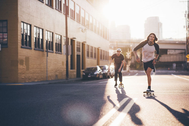 Friends skateboarding on city street against sky during sunny day