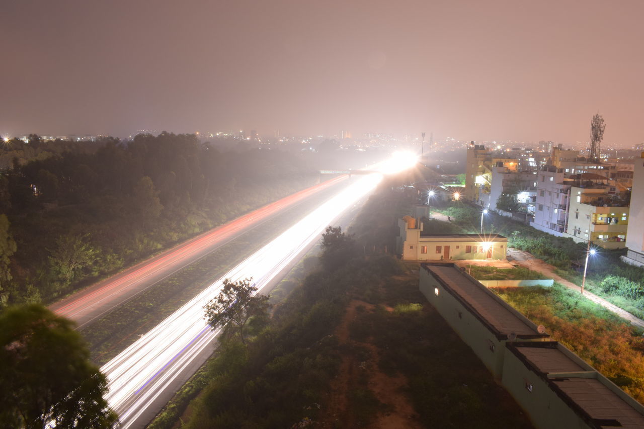 HIGH ANGLE VIEW OF ILLUMINATED ROAD AGAINST SKY IN CITY
