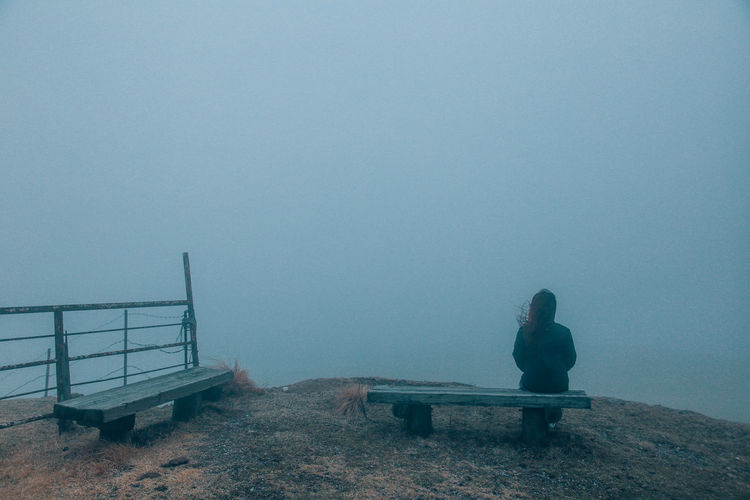 Rear view of woman sitting on bench during foggy weather