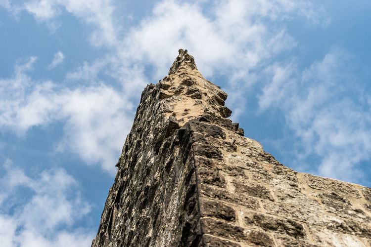 The ruins of a historical tower against a blue sky with white clouds.