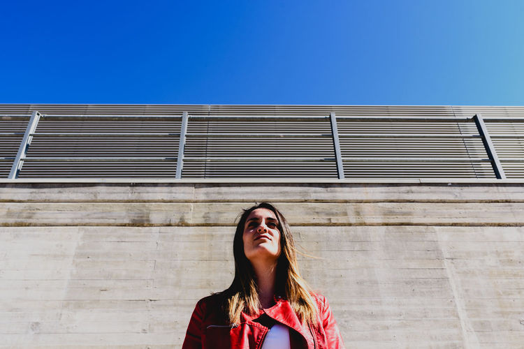 Low angle view of young woman standing against wall