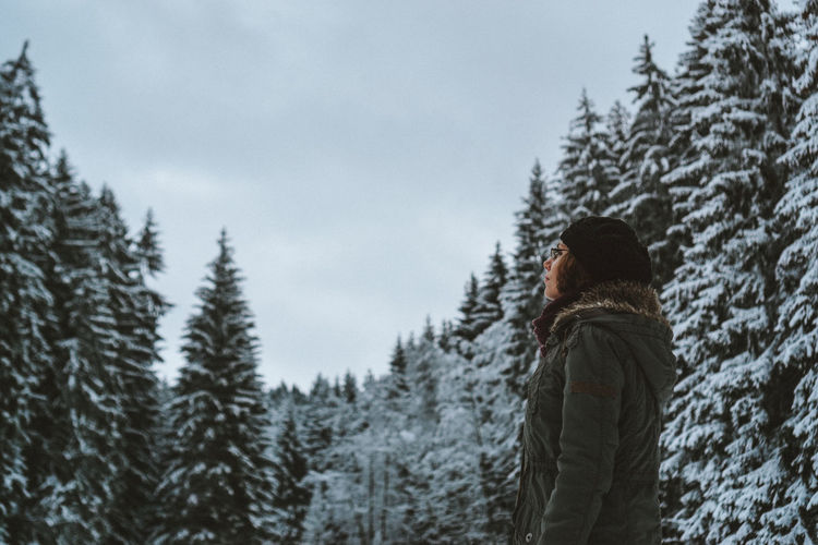Side view of young woman standing against trees during winter