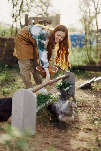 Happy young woman feeding hen on sunny day