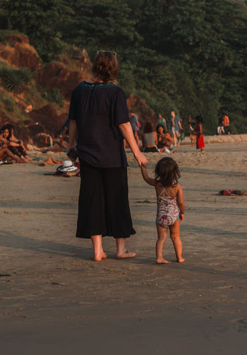 Rear view of mother and daughter holding hands at beach