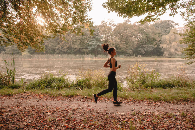 Side view of young woman jogging in forest by lake