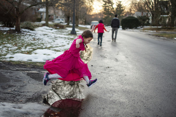 A little girl in long dress leaps across puddle on walk with family