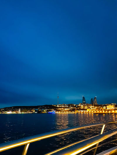 Illuminated city by sea against sky at night