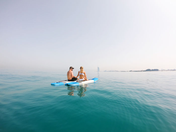 Couple in love sitting on the paddle board  in sea against sky