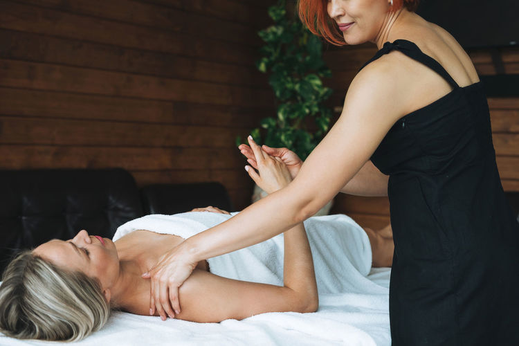 Attractive blonde young woman on couch with white linen enjoys hand body massage in spa