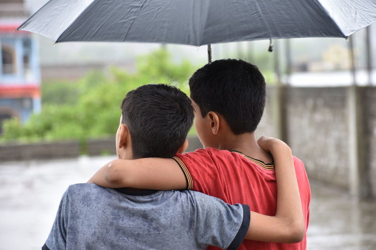 Rear view of brothers with umbrella during rainy season
