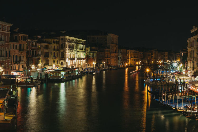 Illuminated buildings by canal in city at night