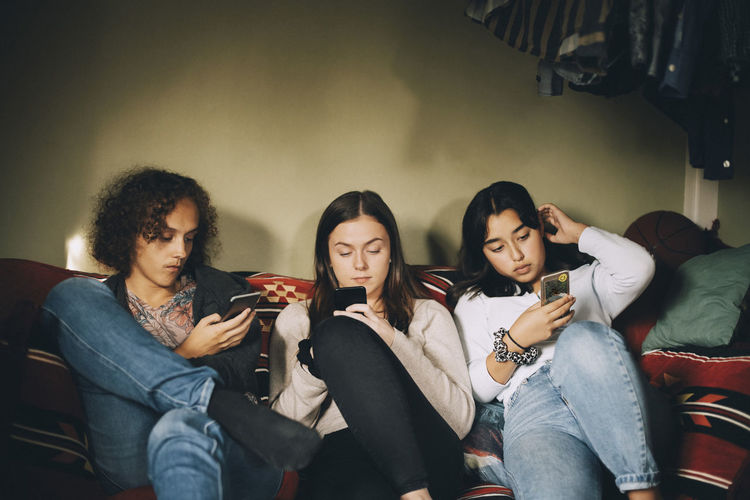 Distracted male and female friends using mobile phones while sitting on sofa at home