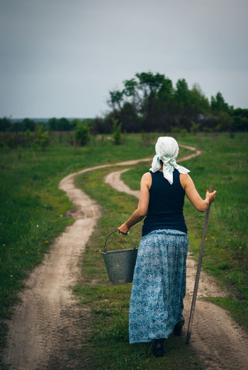 Rear view of woman holding bucket and stick
