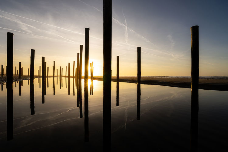 Silhouette wooden posts in lake against sky during sunset